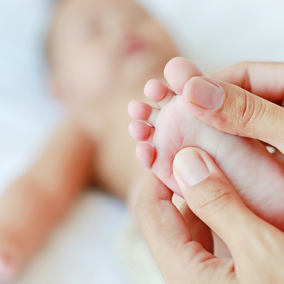 A baby lying on its back and an adult's hands holding one foot